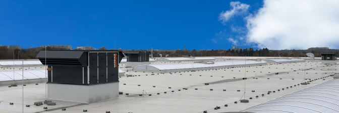 Mehrere RLT-Geräte auf dem Dach eines großen Gebäudes bei blauem Himmel.